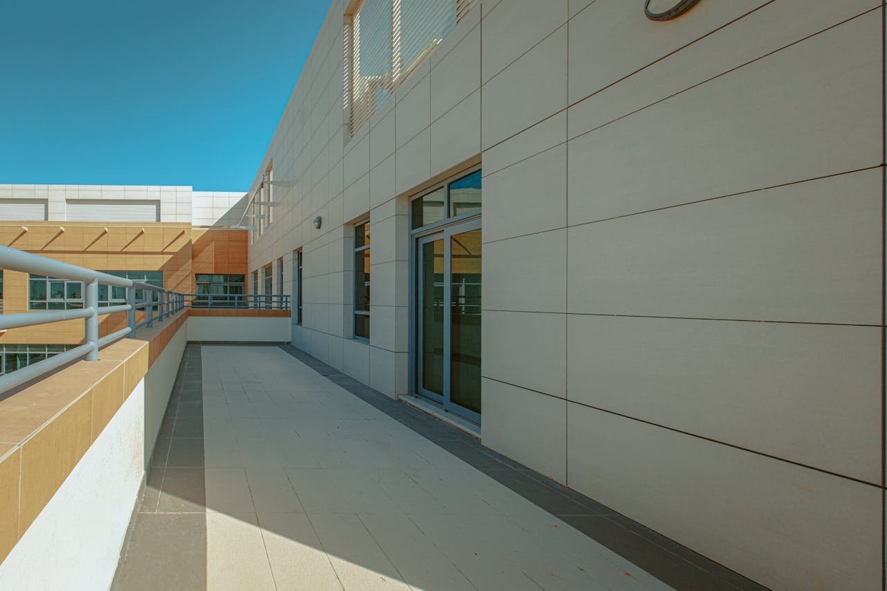 Empty balcony with sliding glass doors on a modern building facade under clear skies.