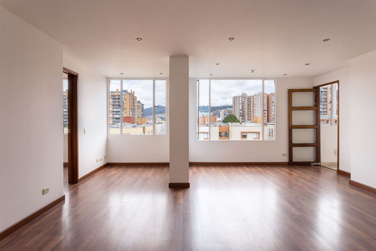 An empty, bright apartment interior showcasing wide windows and wooden flooring.